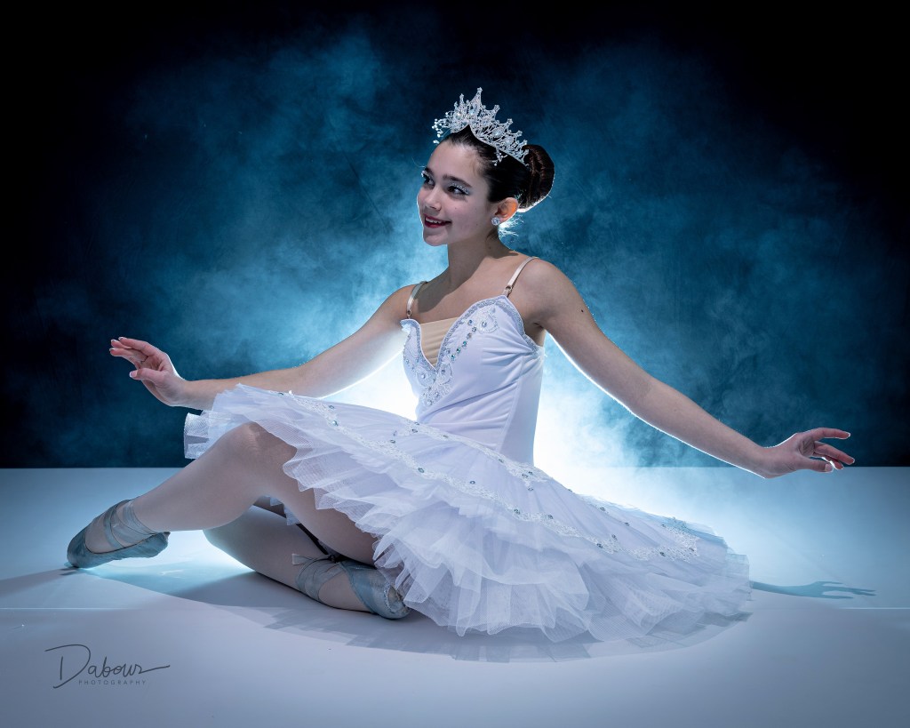 ballet dancer sitting on the floor in white looking to the side with smoke behind her