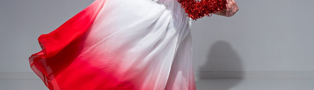 Young dancer in a white and red flowing dress holding a red heart prop in a Valentine themed studio portrait.