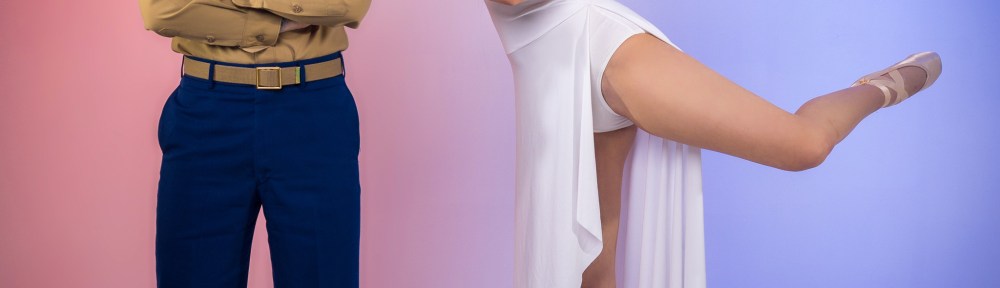 A Marine in a Dress Blue uniform stands next to a ballet dancer in a white dress and pointe shoes performing a tendu, posing together in a studio setting.