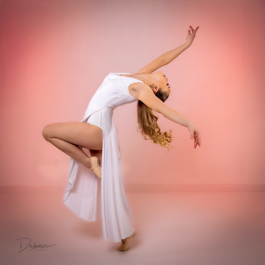 Ballet dancer Addy performing an expressive reaching pose in a white dress