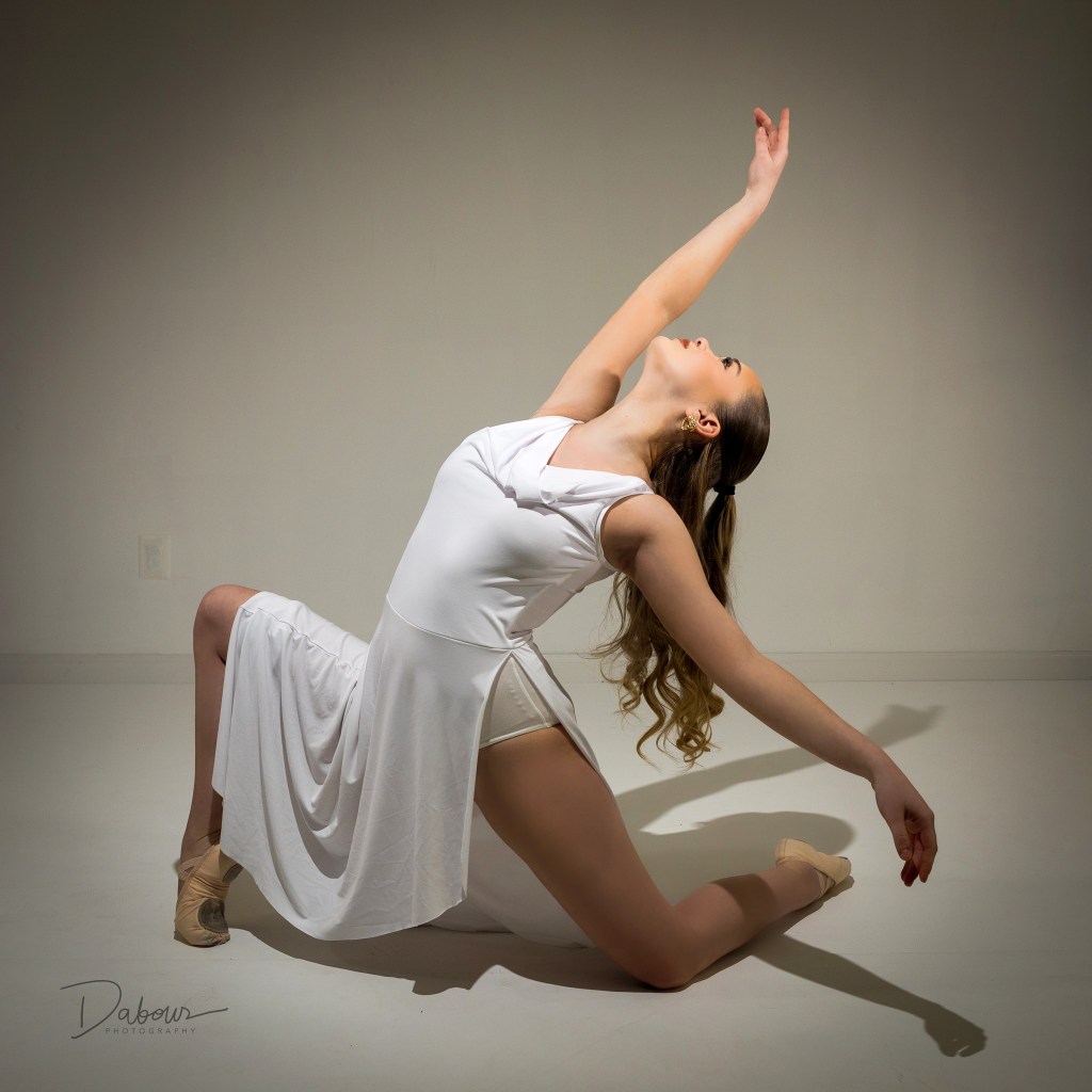 Ballet dancer Addy performing an expressive reaching pose in a white dress