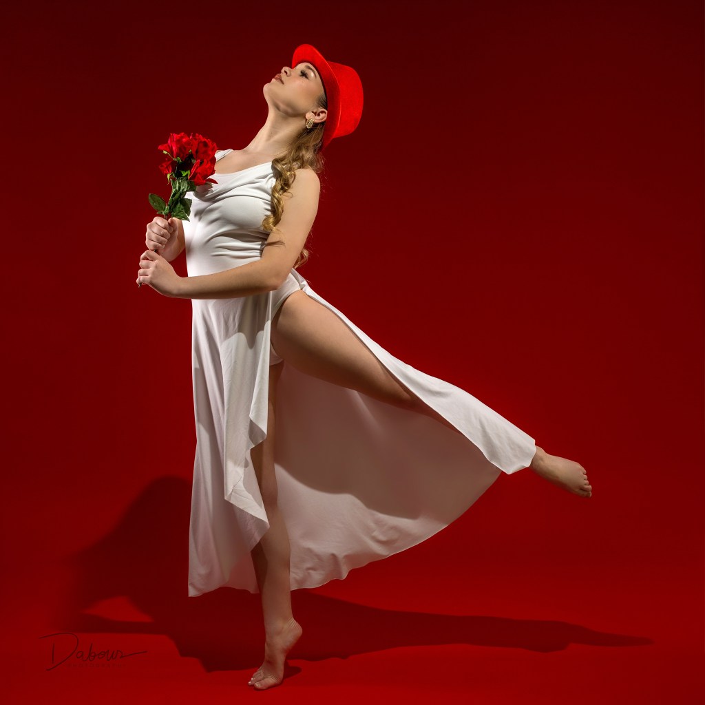 Creative dance portrait of Addy wearing a red top hat and posing on a red background.