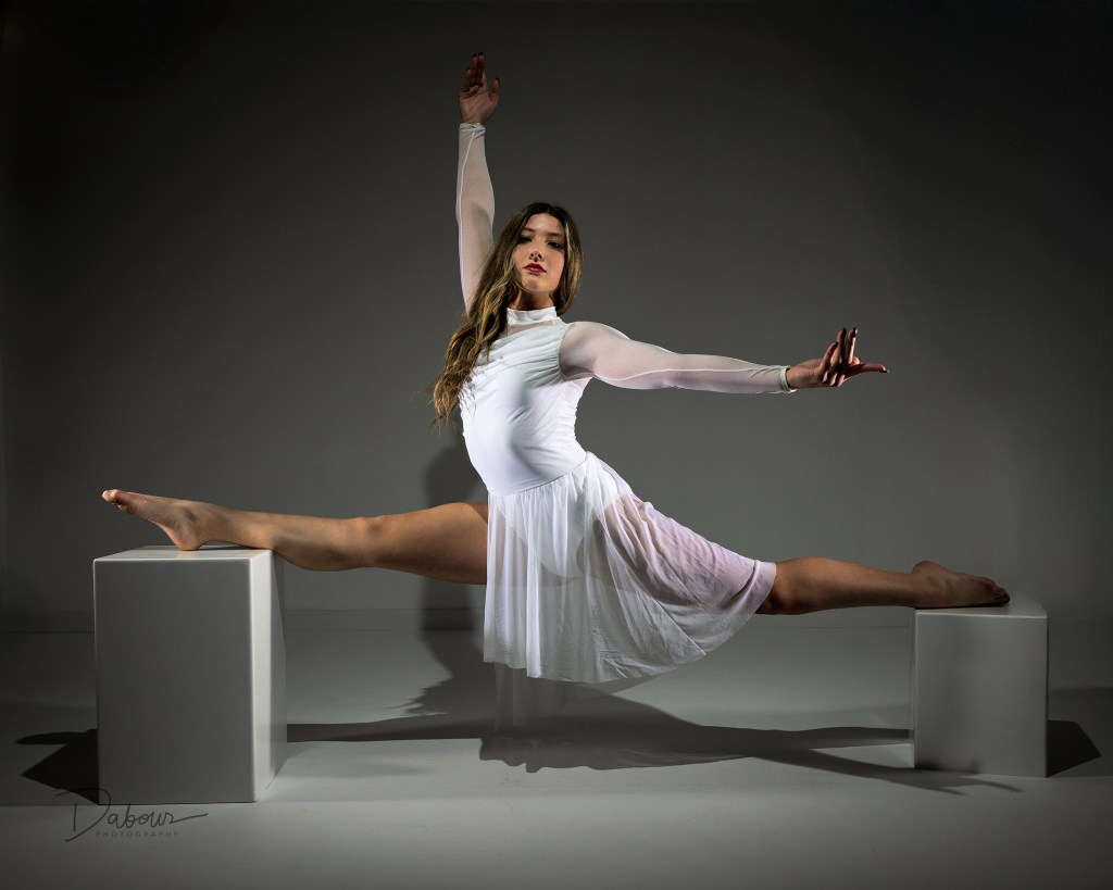 Artistic dance portrait of Mia in a white outfit, performing a strong horizontal pose while balancing with her arms on a white studio block.