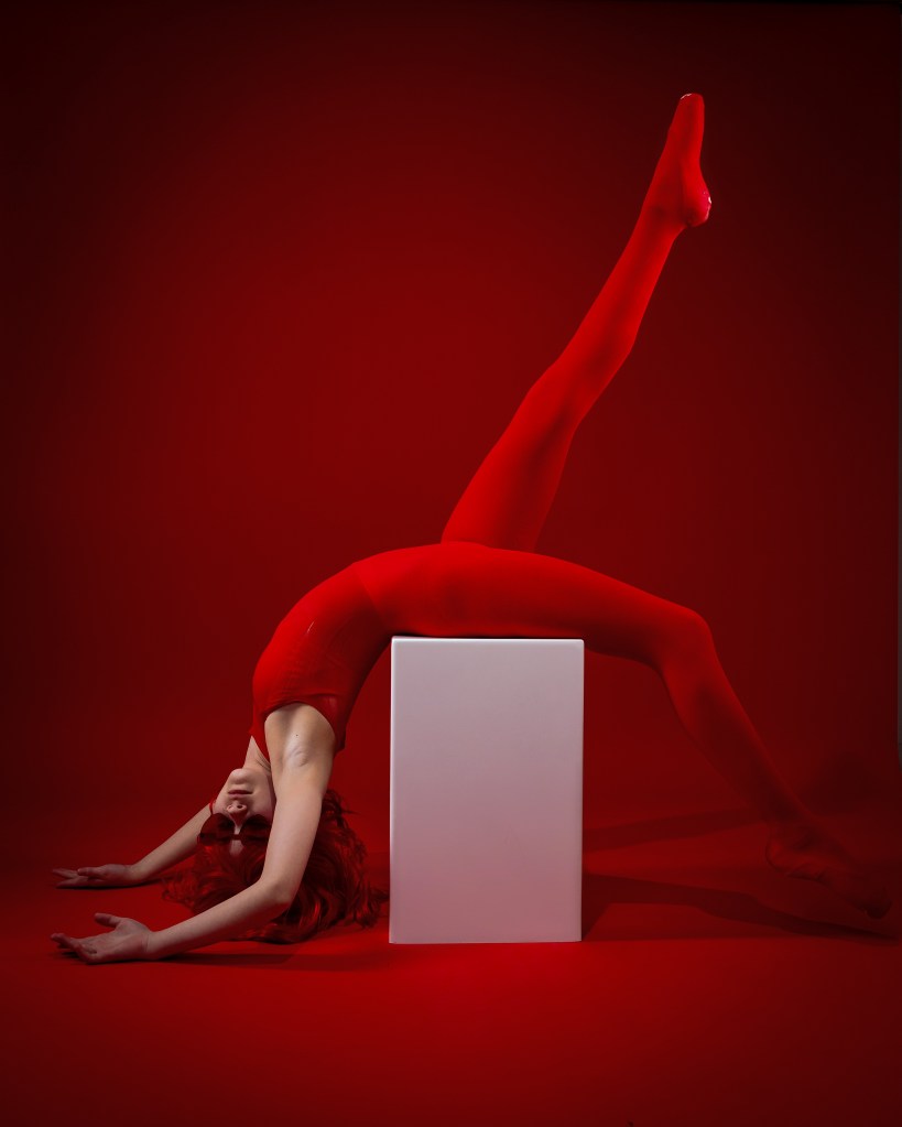 Fine art dance portrait of Ellery in red, showcasing strong lines and dramatic lighting on a red backdrop.
