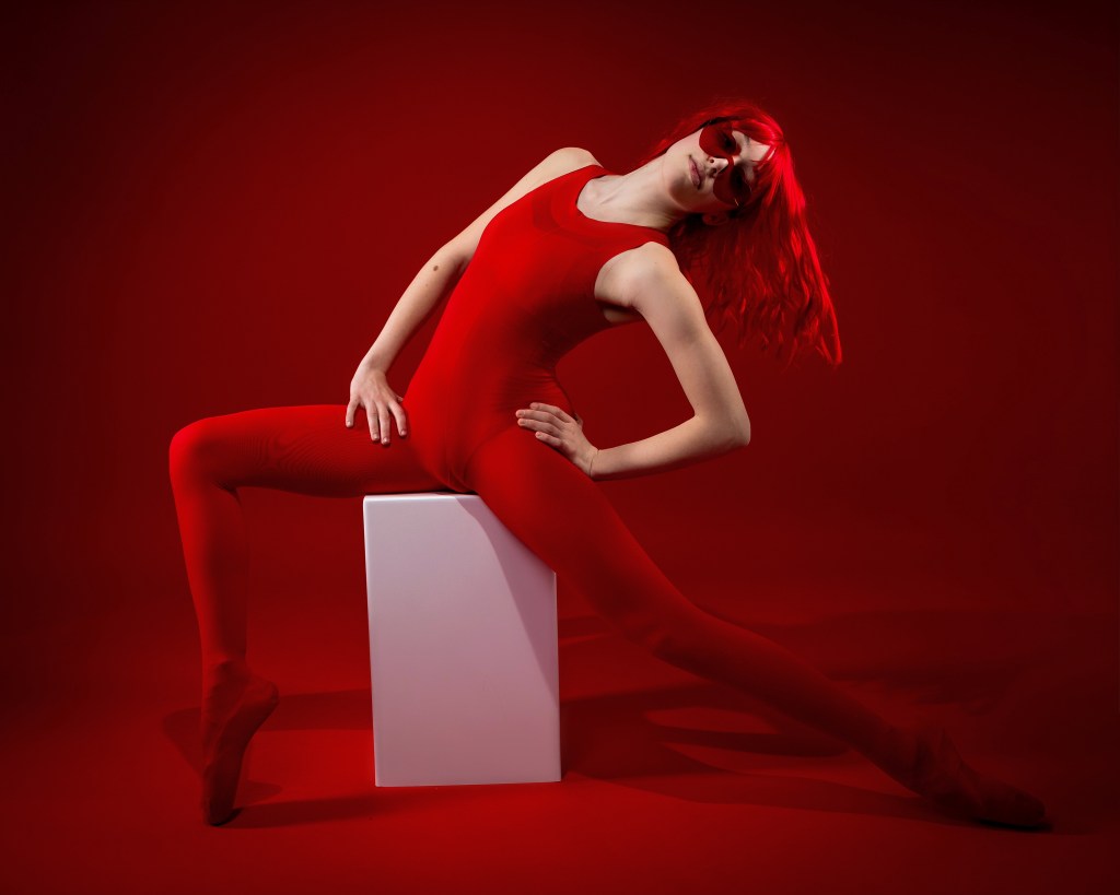 Fine art dance portrait of Ellery in red, showcasing strong lines and dramatic lighting on a red backdrop.