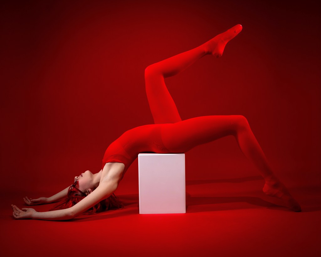 Ellery in a red fashion dance outfit posing on a white block, high-fashion dance photography