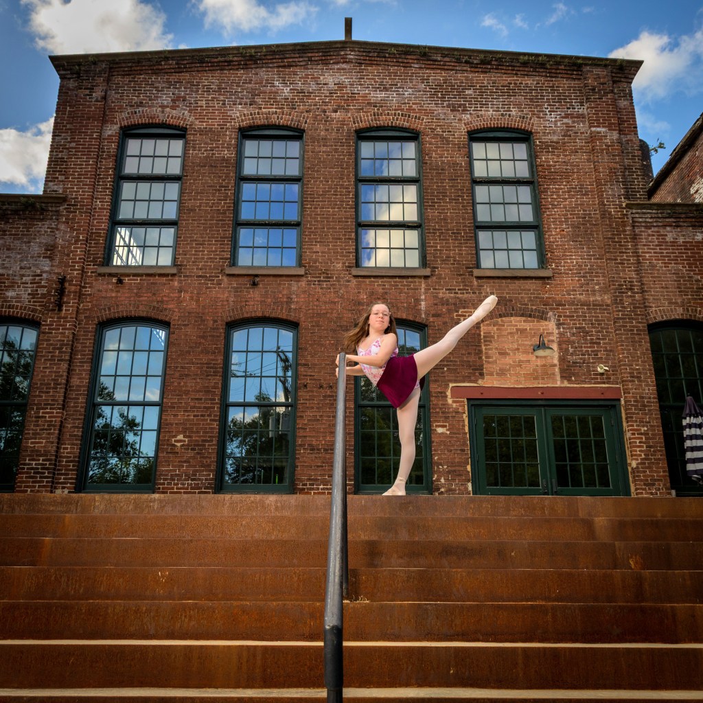 Ballerina Olivia Klein performing a graceful dance pose on an elevated stone ledge at the historic Simon Silk Mill in Easton, PA.