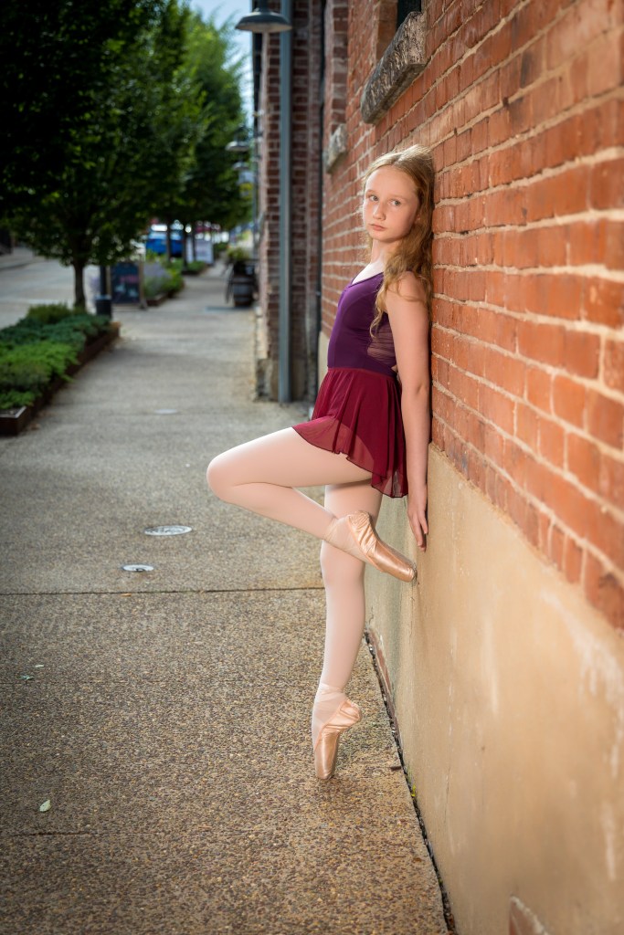 Lily posing at the Easton Silk Mill. She is on pointe, wearing a maroon leotard
