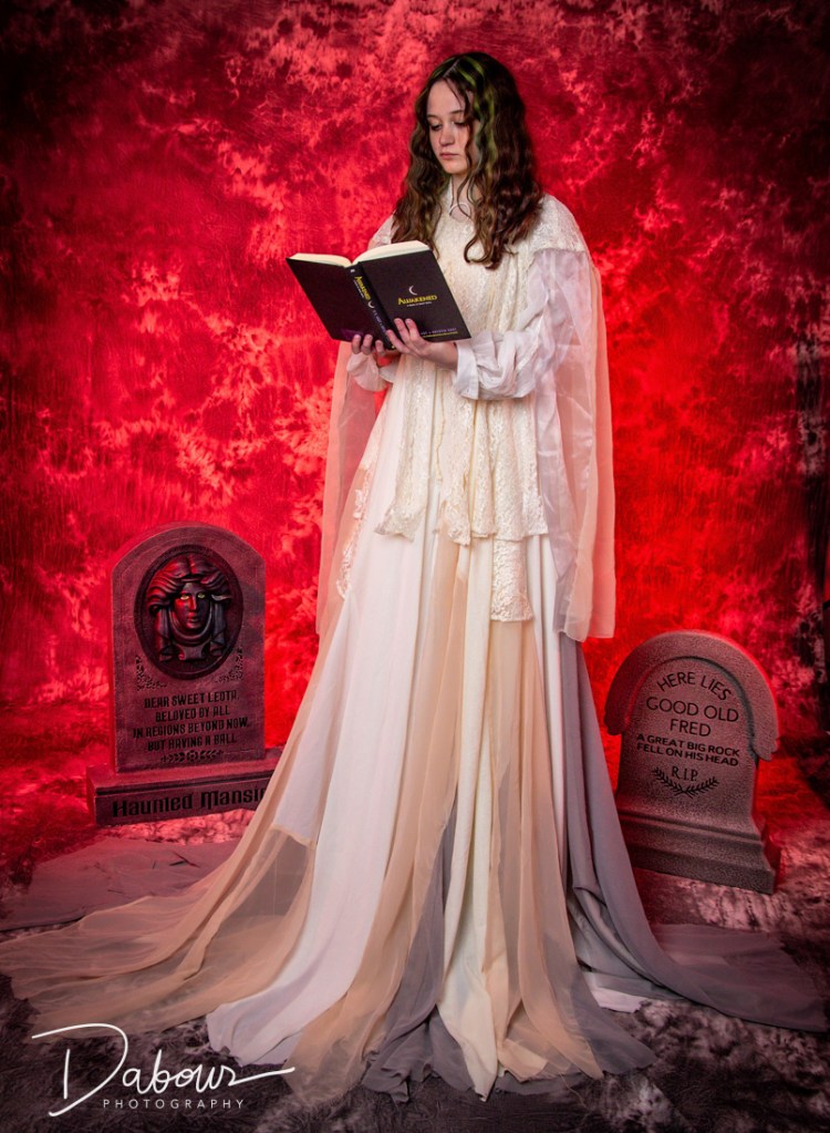 A dancer in a white vintage dress holding a book, posed in a moody, red-lit "spooky" studio setting with a dark backdrop.