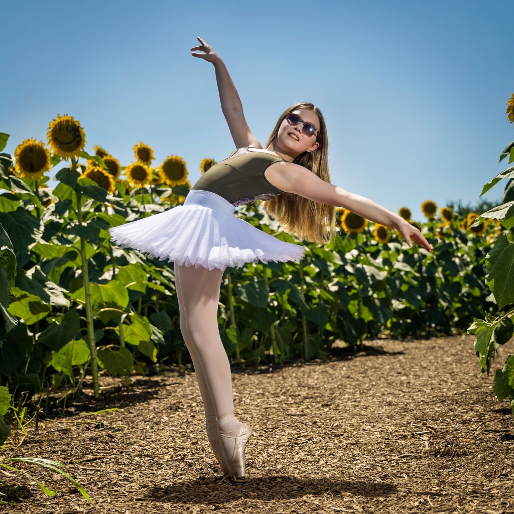 Dance ambassador Vivi Taggart posing in a vibrant yellow sunflower field wearing a black leotard.