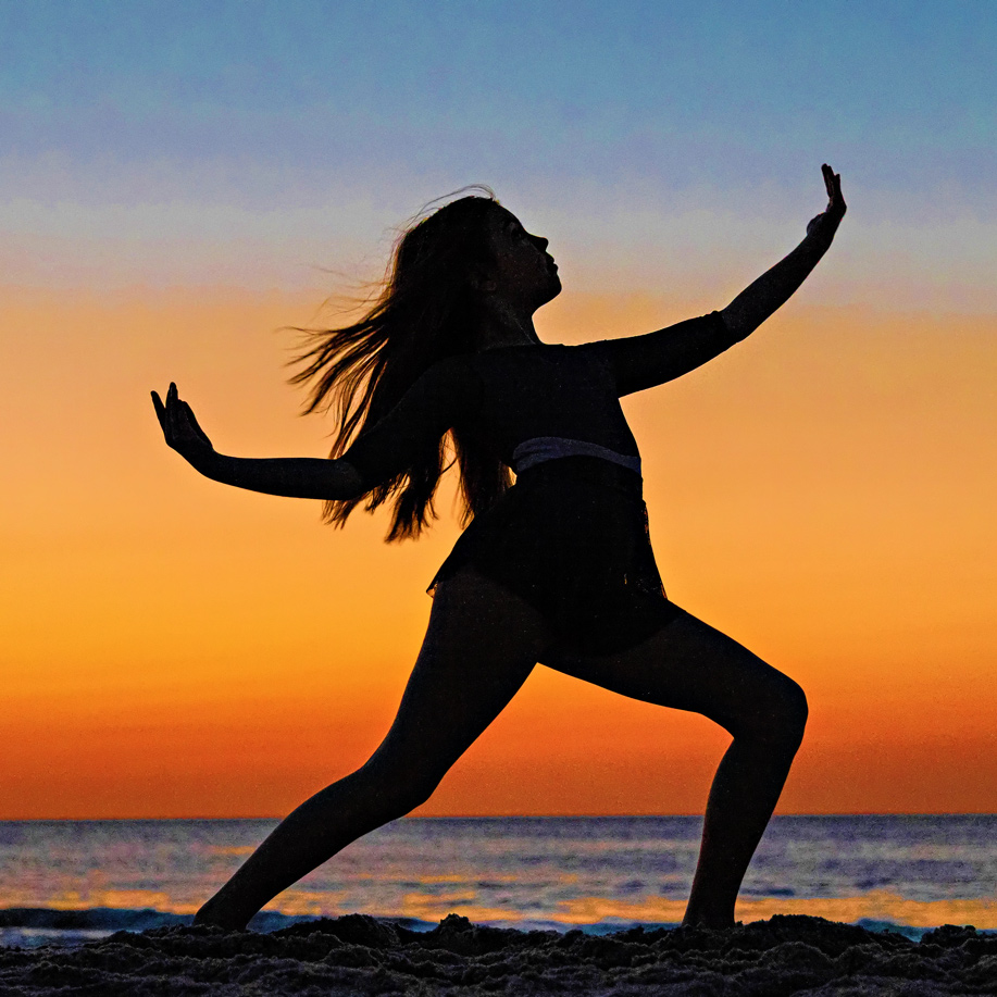 Silhouette of a ballerina performing a pose against a dramatic orange and purple sunrise sky.