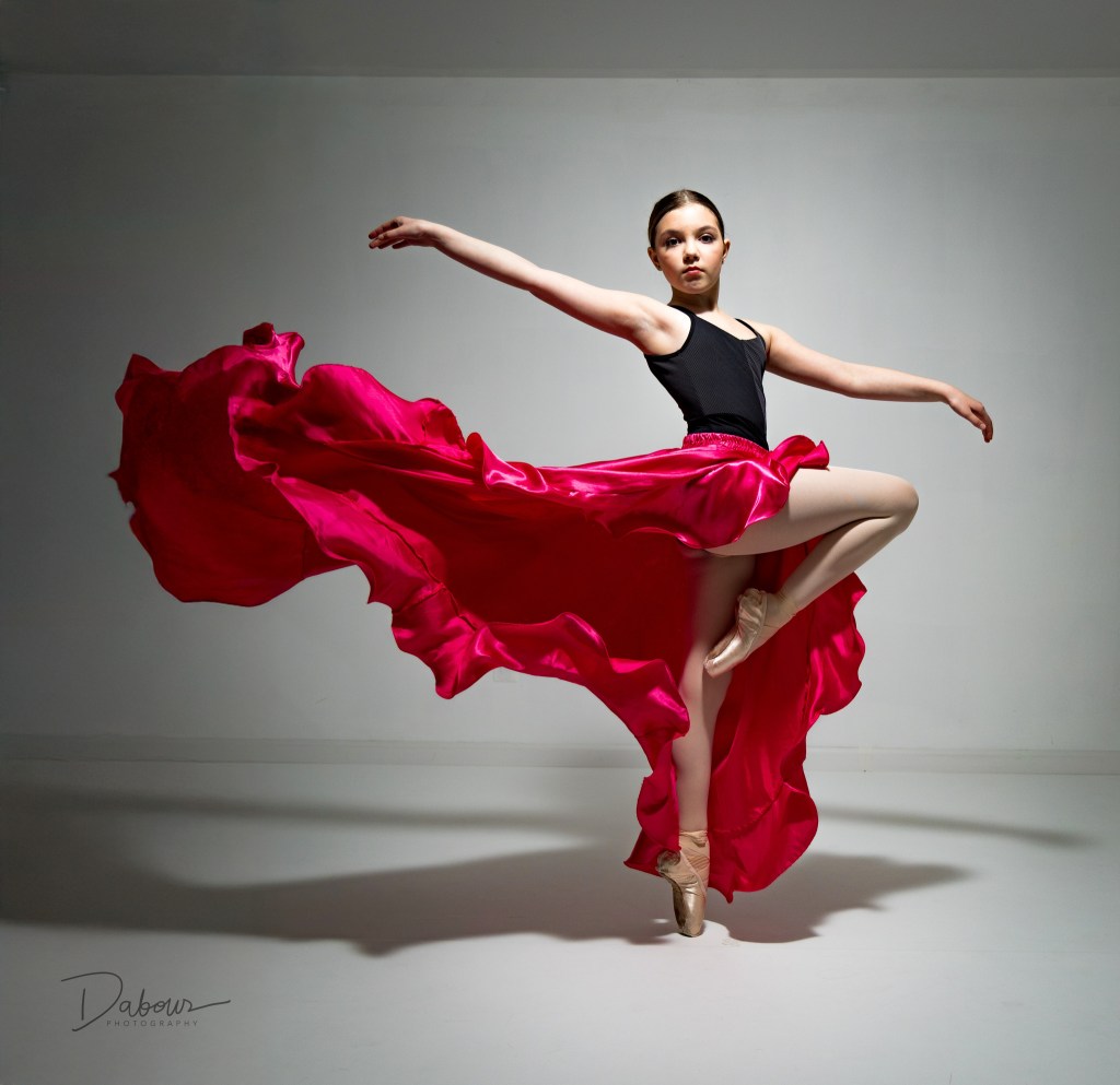 Ballerina Vivi Taggart performing a graceful pose with a long red skirt