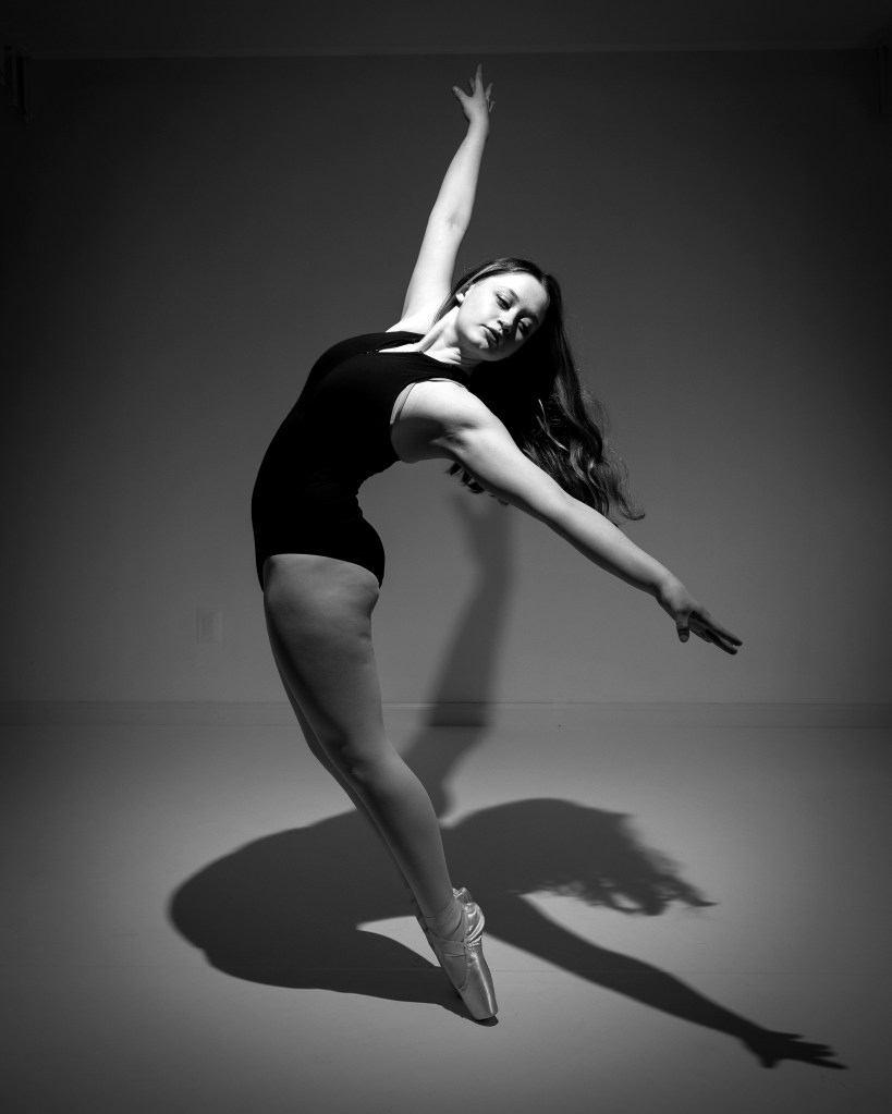 A professional black and white dance audition portrait of Zoey, featuring a dramatic side-profile pose with an arched back and artistic hand positioning against a neutral studio background.